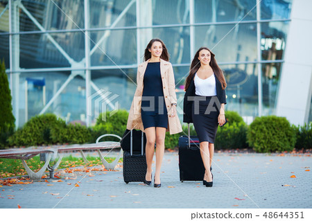 Vacation. Two happy girls traveling abroad together, carrying suitcase luggage in airport 48644351