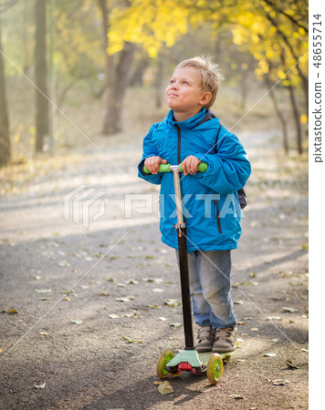 A boy riding a scooter in the autumn park. 48655714