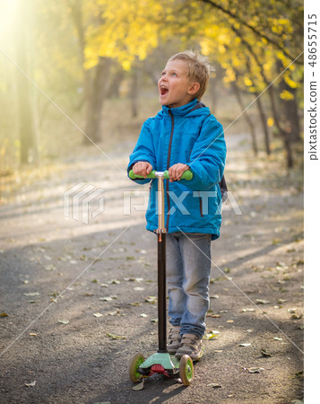 A boy riding a scooter in the autumn park. A boy riding a scooter in the autumn park. 48655715