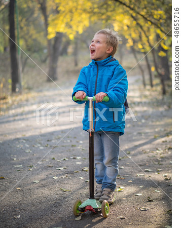 A boy riding a scooter in the autumn park. A boy riding a scooter in the autumn park. 48655716