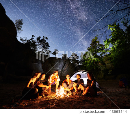Friends hikers resting beside camp, campfire, tent at night 48665344