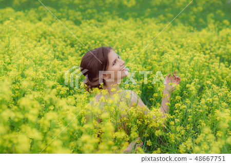 Young beautiful girl in field with yellow flowers Young beautiful girl in field with yellow flowers 48667751