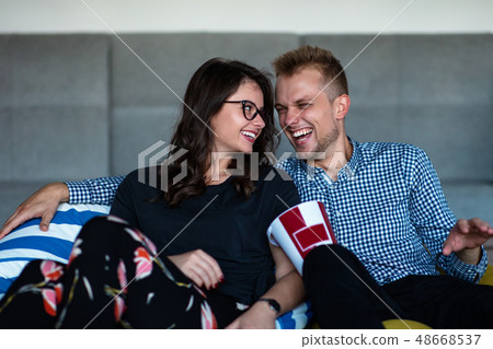 Portrait of an excited young couple relaxing on a couch at home while watching TV and eating popcorn 48668537
