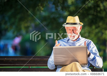 Senior man using laptop computer at rest in the park outdoors Senior man using laptop computer at rest in the park outdoors 48668671