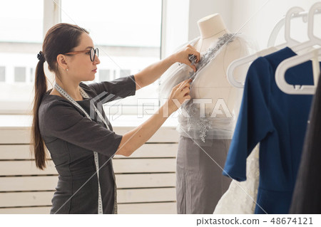 Dressmaker, tailor, fashion and showroom concept - Side view of female fashion designer measuring Dressmaker, tailor, fashion and showroom concept - Side view of female fashion designer measuring 48674121