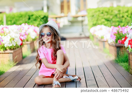 Fashion little girl model wearing a pink checkered shirt, hat and sunglasses in city 48675492