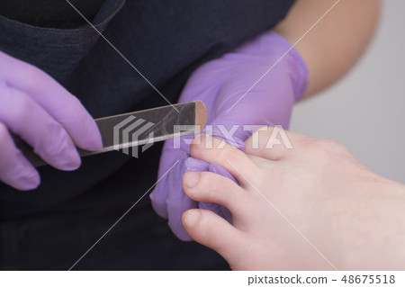 Processing toenails. Gloved hands with a nail file Processing toenails. Gloved hands with a nail file 48675518
