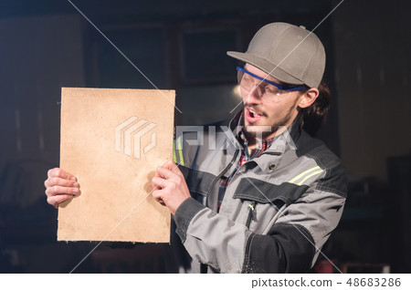 Portrait of a young carpenter in overalls and goggles with a mock up board holding a blank sign in Portrait of a young carpenter in overalls and goggles with a mock up board holding a blank sign in 48683286