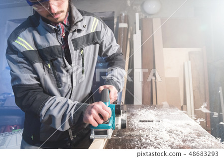A young carpenter with a beard works with an electric plane without suctioning sawdust. Leveling and 48683293
