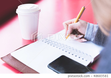 Close-up from behind the back of a young woman in a winter polto is holding a ballpoint pen and is 48683581
