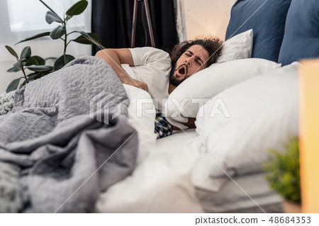Sleepy young man yawning in the bed Sleepy young man yawning in the bed 48684353