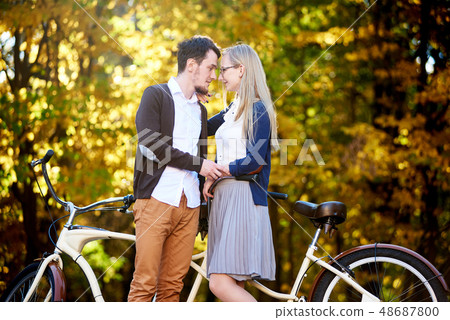 Young romantic couple bearded man and attractive woman at tandem bicycle in autumn park or forest. 48687800