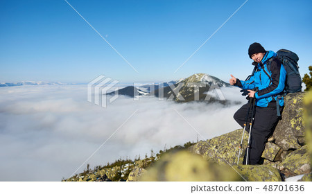 Hiker man on rocky hill on foggy valley with white clouds, snowy mountains and blue sky background. Hiker man on rocky hill on foggy valley with white clouds, snowy mountains and blue sky background. 48701636