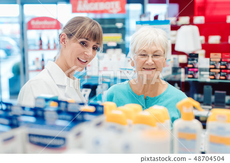 Chemist and customer standing in pharmacy between the shelves 48704504