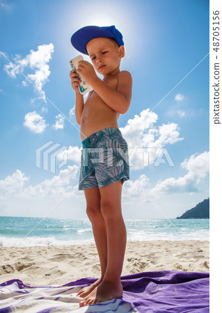 Cute boy is playing in a mobile phone on the beach Cute boy is playing in a mobile phone on the beach 48705156