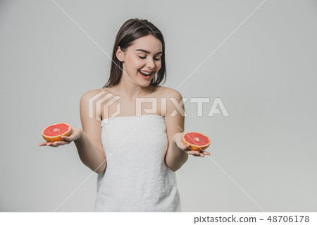 Happy young girl posing with fruit. Slices of red grapefruit in her hands on a white background 48706178