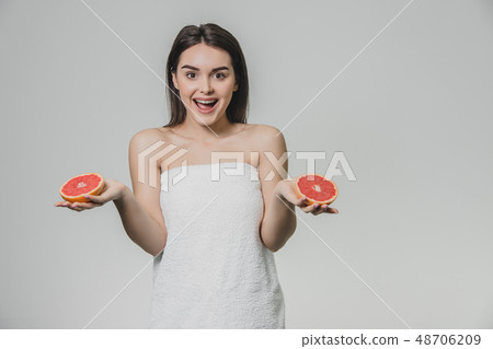 Happy young girl posing with fruit. Slices of red grapefruit in her hands on a white background Happy young girl posing with fruit. Slices of red grapefruit in her hands on a white background 48706209