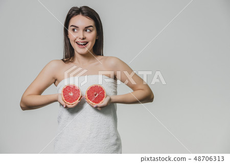 Happy young girl posing with fruit. Slices of red grapefruit in her hands on a white background Happy young girl posing with fruit. Slices of red grapefruit in her hands on a white background 48706313
