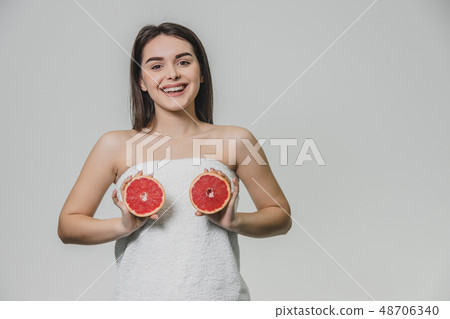 Happy young girl posing with fruit. Slices of red grapefruit in her hands on a white background Happy young girl posing with fruit. Slices of red grapefruit in her hands on a white background 48706340