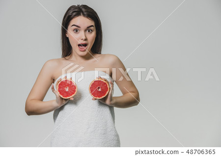Happy young girl posing with fruit. Slices of red grapefruit in her hands on a white background Happy young girl posing with fruit. Slices of red grapefruit in her hands on a white background 48706365