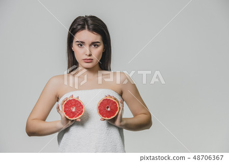 Happy young girl posing with fruit. Slices of red grapefruit in her hands on a white background 48706367