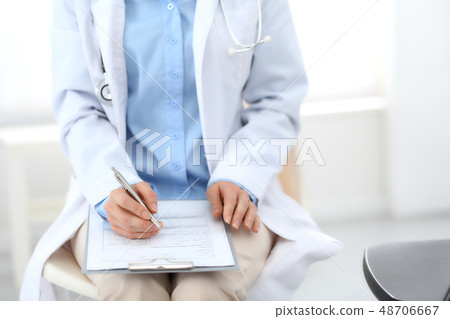 Female doctor writing up medication history records form on clipboard, while sitting at the chair 48706667