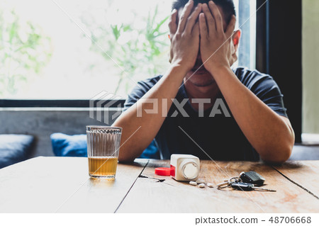 Depression man hand on his face with glass of alcohol and pills on the table. 48706668