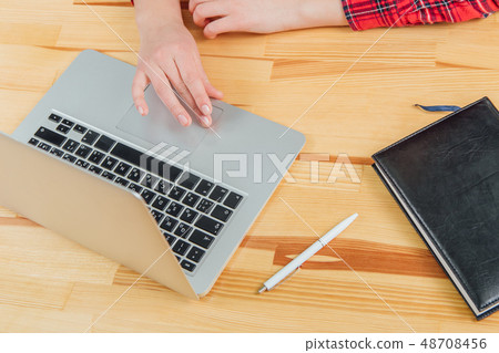 Workspace with laptop, women's hands, gray notebook, white pen and black pad on the table. Flat 48708456