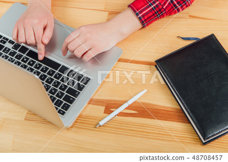 Workspace with laptop, women's hands, gray notebook, white pen and black pad on the table. Flat Workspace with laptop, women's hands, gray notebook, white pen and black pad on the table. Flat 48708457