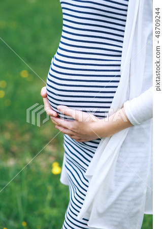 Pregnant young woman touching her big belly and walking in the park 48709244