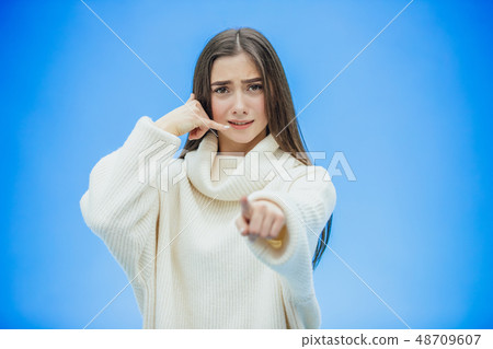 Beautiful young girl on a blue background. The girl shows a phone call with a gesture. Dressed in a Beautiful young girl on a blue background. The girl shows a phone call with a gesture. Dressed in a 48709607