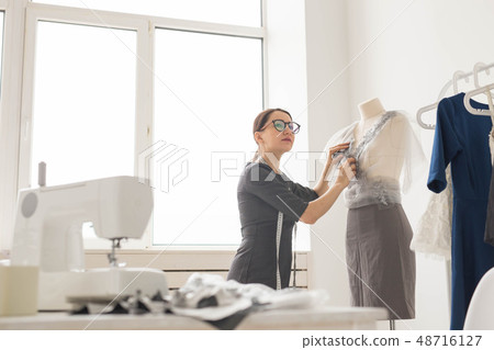 Dressmaker, tailor, fashion and showroom concept - Side view of female fashion designer measuring Dressmaker, tailor, fashion and showroom concept - Side view of female fashion designer measuring 48716127