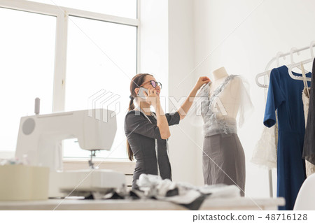 Dressmaker, tailor, fashion and showroom concept - beautiful young designer is talking on the mobile Dressmaker, tailor, fashion and showroom concept - beautiful young designer is talking on the mobile 48716128