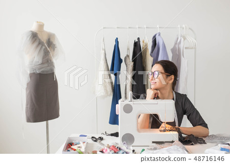 Dressmaker, tailor and fashion concept - Smiling female fashion designer using sewing machine and Dressmaker, tailor and fashion concept - Smiling female fashion designer using sewing machine and 48716146