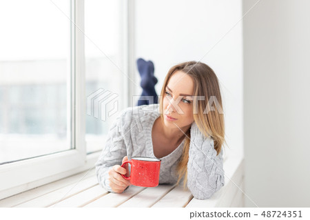 People and fashion concept - Portrait of beautiful woman in knitted dress lying on a sill with red People and fashion concept - Portrait of beautiful woman in knitted dress lying on a sill with red 48724351