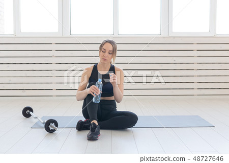 People, sport and fitness concept - young woman drinking water from sportive bottle while sitting on People, sport and fitness concept - young woman drinking water from sportive bottle while sitting on 48727646