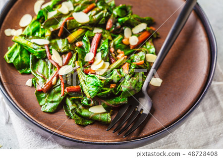Beet greens salad with nuts in black plate. 48728408