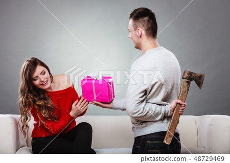 Insincire man holding axe giving gift box to woman Insincire man holding axe giving gift box to woman 48729469