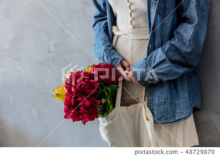 Female hands holding bouquet of peonies and  Leucadendron in a tote bag 48729870