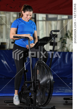 Pregnant woman doing intense workout at gym air bike 48733648