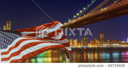 Brooklyn Bridge closeup over East River at night in New York City Manhattan and American flag flying Brooklyn Bridge closeup over East River at night in New York City Manhattan and American flag flying 48734088