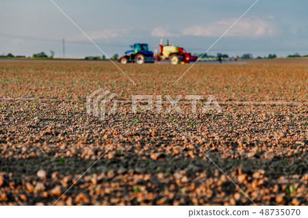 Agricultural worker with tractor working in field. 48735070