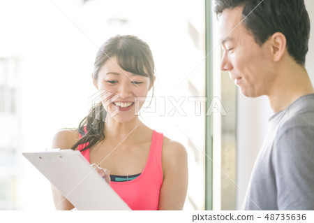 A man who is shown a muscle training menu from a female instructor at a personal gym and receives explanation A man who is shown a muscle training menu from a female instructor at a personal gym and receives explanation 48735636