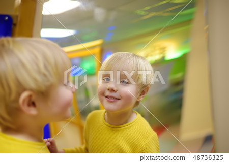 Cute little boy looks in distorting mirror Cute little boy looks in distorting mirror 48736325