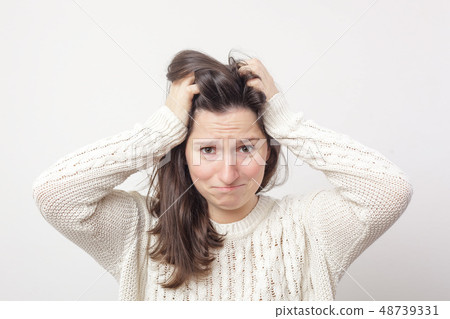 Girl in a white sweater desperately grabs her head 48739331