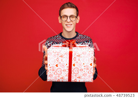 A man with glasses holds out a gift box A man with glasses holds out a gift box 48739523