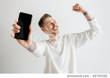 Young handsome man showing smartphone screen isolated on gray background in shock with a surprise 48740360