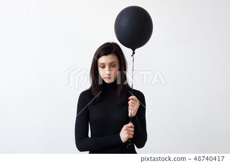 A sad girl holds a black balloon in her hands. 48740417