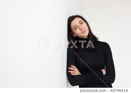 A girl in black clothes is standing by white wall. A girl in black clothes is standing by white wall. 48740418