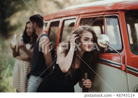 A group of friends standing outdoors on a roadtrip through countryside, holding bottles. 48743114